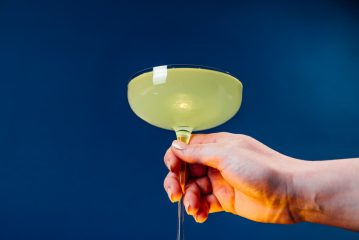 Hand holds a light yellow-green cocktail in a coupe glass