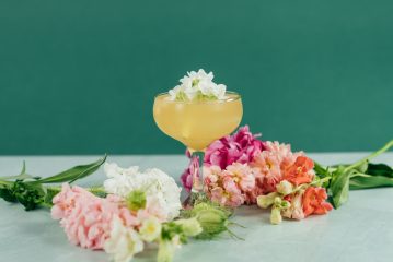 A yellow cocktail surrounded by flowers acts as a centerpiece in a DIY cocktail bar
